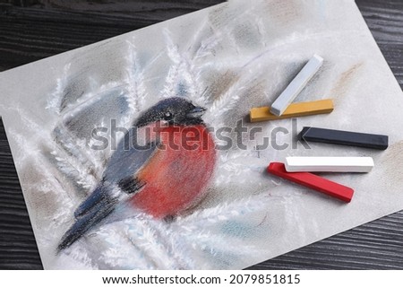 Colorful chalk pastels and beautiful painting of bullfinch on black wooden table, top view