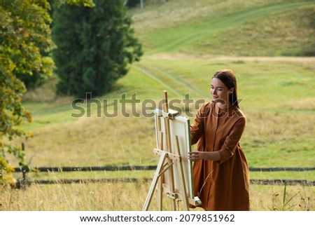 Beautiful young woman drawing on canvas in nature. Space for text
