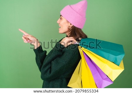 Young woman on a green background in a warm cozy sweater and a pink hat with colored shopping bags