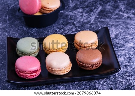 Different macarons of different flavors on a black plate.