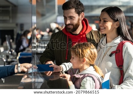 Unrecognizable employee of airport checking passports and biometric data while working with family of passengers. Happy parents and their daughter having trip 
