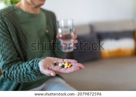 Cropped view of sick and ill mature aged woman holding different pills on palm hand, showing medical preparat on camera