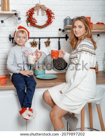 Pregnant mother and her son enjoying in kitchen and christmast time. Pregnant woman with son on New Year's holidays.