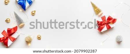 Winter background gold. White gift with red bow, gold balls and sparkling lights garland in xmas decoration on white background for greeting card. Winter festive composition with copy space