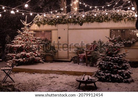 Mobile home Caravan with terrace at night, Mobile home decorated with Christmas decor. Festive atmosphere - lights, blankets, Christmas trees. Caravan camping. mobile home trailer. Selective focus