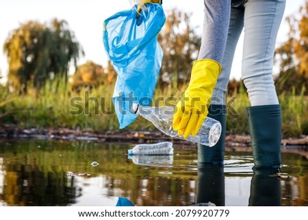 Volunteer picking up plastic bottle from polluted lake or river. Water pollution with plastic garbage. Environmental damage Royalty-Free Stock Photo #2079920779