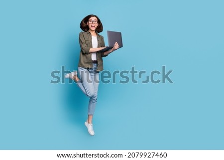 Full length photo of excited lady computer geek it developer jump use gadget wear shirt denim jeans isolated over blue color background
