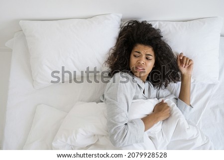Sleep deprivation, insomnia. Top above view of female looks over her shoulder aside, wakes up from the noise. Tired african american woman lying on uncomfortable bed in pajamas making disgruntled face Royalty-Free Stock Photo #2079928528