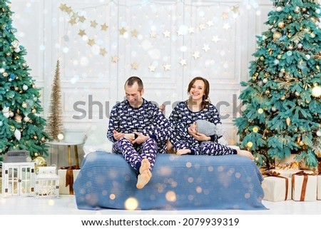 Happy family in pajamas enjoyng love hugs indoors in light enterior room near decorated Christmas tree.