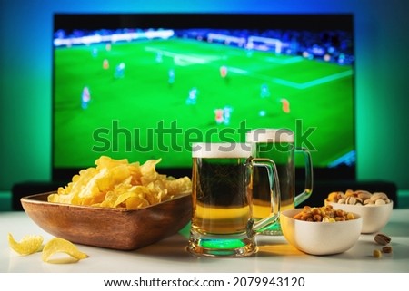 Beer and snacks set on football match tv background.