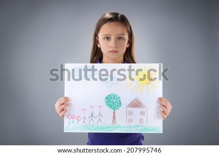 sad little girl holding picture. cute kid standing on grey background