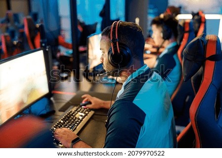 Rear view of cybersport gamer wearing headphones playing online video game while participating in esports tournament in internet cafe