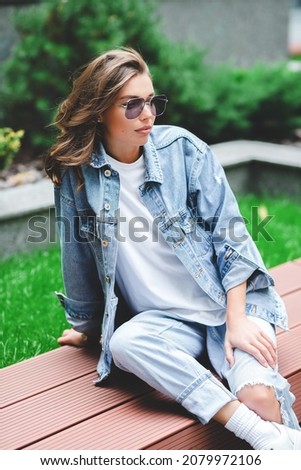 Hipster girl in clean white t-shirt and jeans posing against the background of buildings, minimalist urban clothing style