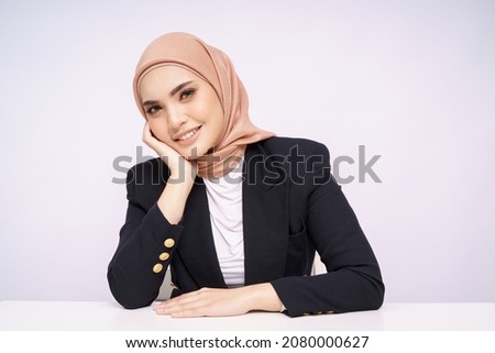 A beauty shot of a pretty young Asian hijab corporate girl with smooth glowing skin smiling and relaxing on a table over white background studio. Beauty skin care, office concept. Royalty-Free Stock Photo #2080000627