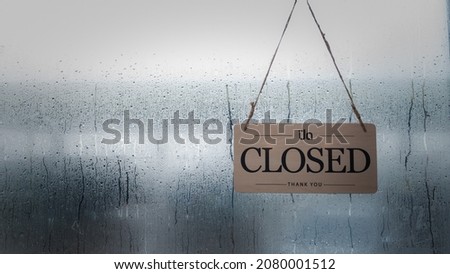 A closed sign hanging in front of a shop window on a rainy day.copy space.