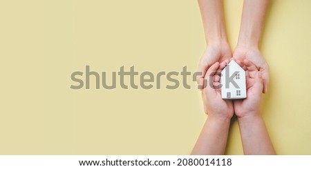 Mother and son hand holding wooden house on yellow background, homeless housing and home protecting insurance concept, international day of families, homeschooling, Top view.	
