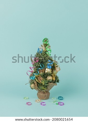 A small fir tree decorated with toys and streamers on a blue background. The minimum concept of the New Year. Contemporary art. Place for text.
