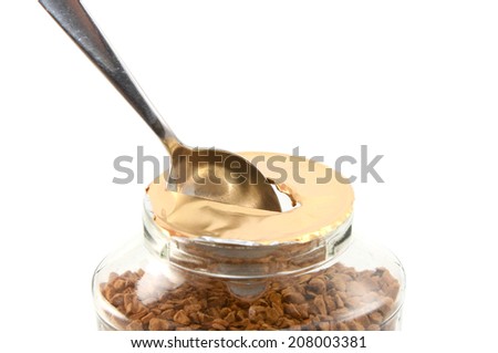 Ripping a hole in the foil of a new jar of instant coffee granules with a teaspoon, isolated on a white background