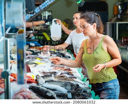 Cheerful women looking for fresh marine products on icy showcase of seafood market