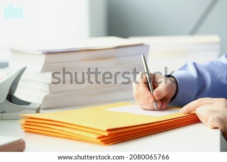 Man with pen in hand signing envelope while sitting at table with bunch of documents