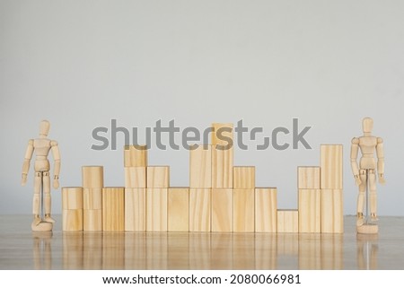 2 wooden dolls and wooden blocks on a table that line together like a graph. White background . Construction business risk concept.