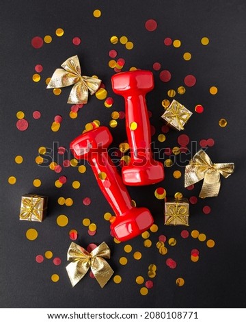 Exercises, fitness and development of the concept of a merry Christmas and a happy New Year. Red dumbbells, bows and gifts with ribbons on a black background. Flat lay, top view. Vertical photography