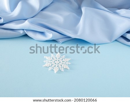 Modern creative Christmas composition with white snowflake on pastel blue background against shiny blue curtain. Creative New Year concept with copy space.