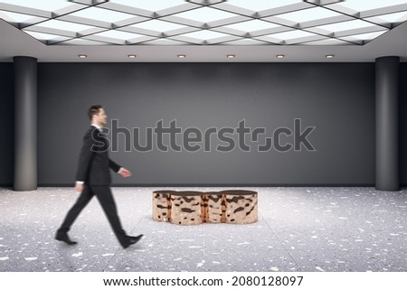 Man walking in modern exhibition hall interior with shiny golden seat and empty mock up place on concrete wall. Gallery and art concept