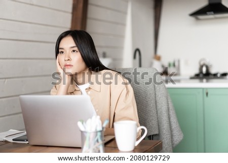 Bored asian girl student working on laptop, looking into distance with sad gloomy face, sitting at home, studying online