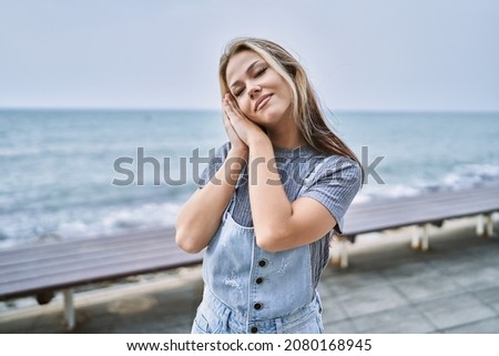 Young caucasian woman outdoors sleeping tired dreaming and posing with hands together while smiling with closed eyes. 