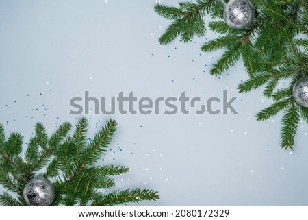 Festive Christmas background. Silver ornaments, star confetti and natural green fir tree on light blue background. New year postcard. Winter holiday layout composition. Copy space, flat lay, top view.