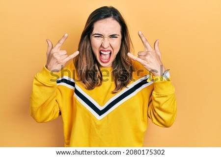 Young hispanic girl wearing casual clothes shouting with crazy expression doing rock symbol with hands up. music star. heavy music concept. 