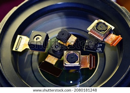 Miniature photo and video cameras of smartphones lie on the lens of the standard lens of a reflex camera for a visual assessment of their size