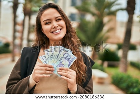 Young hispanic woman smiling happy holding romania leu banknotes at the city. Royalty-Free Stock Photo #2080186336