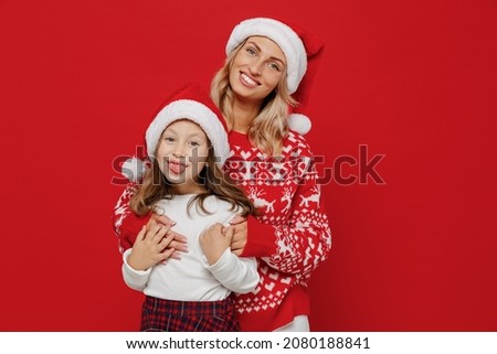 Young cheerful woman in sweater have fun with child baby girl 6-7 years old. Mommy little kid daughter hugging show tongue isolated on plain red color background studio. New Year love family concept