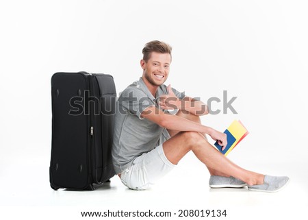 handsome guy sitting on floor and smiling. profile of man with luggage on white background