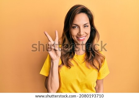 Young latin woman wearing casual clothes showing and pointing up with fingers number two while smiling confident and happy.  Royalty-Free Stock Photo #2080193710