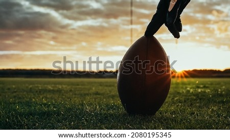 American Football Kickoff Game Start. Close-up Shot of an American Ball Standing on a Grass Field Held by Professional Player. Preparation for Championship Game. Royalty-Free Stock Photo #2080195345