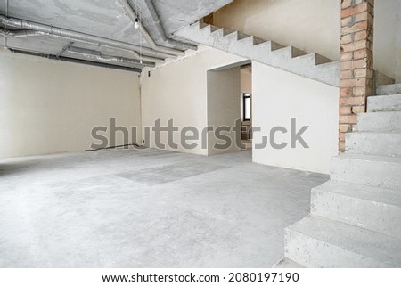 The room is under construction with a rough finish, plastered walls, concrete floor. Wiring of ventilation pipes on a concrete ceiling in a house under construction. Royalty-Free Stock Photo #2080197190