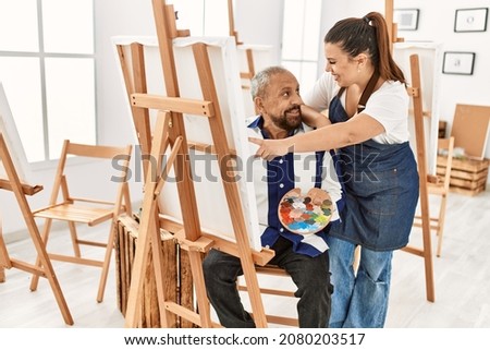 Young painting teacher woman teaching art to senior man painting on canvas at art studio
