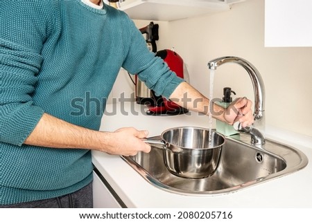 Young man with arms rolled up filling a container with water to boil spaghetti