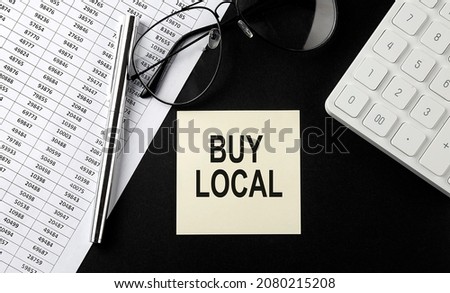 Concept BUY LOCAL message on sticker with glasses,chart and calculator on black background