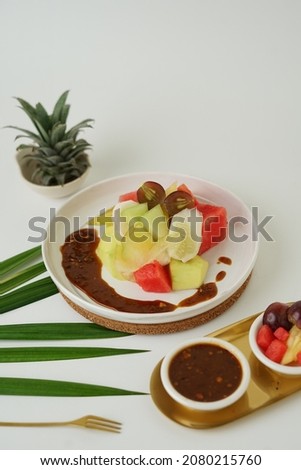 Rujak Buah or Tropical Fresh Fruit Salad with Spicy Coconut Sugar Dressing on white oval plate.