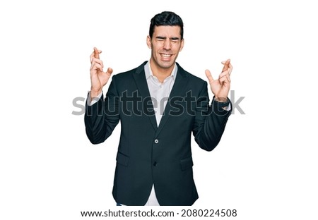 Handsome hispanic man wearing business clothes gesturing finger crossed smiling with hope and eyes closed. luck and superstitious concept. 