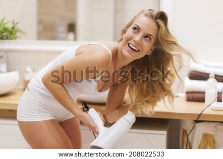 Blonde woman has fun during drying hair in bathroom  