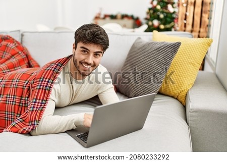 Young hispanic man smiling happy lying on the sofa using laptop at home.