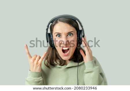 Young woman listens to music in headphones on a gray background , shows a sign of heavy metal with her hands.