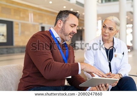 General practitioner discussing patient case status with his medical staff using digital tablet. Pharmaceutical representative showing medical report on digital tablet to mature doctor. Royalty-Free Stock Photo #2080247860