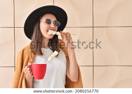 Beautiful young woman with cup of coffee and marshmallows on color background