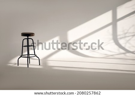 A white room with a shade from the sun through the window and one high bar stool. Minimalism style in horizontal photography. Loneliness concept with one chair and white space with shadows Royalty-Free Stock Photo #2080257862